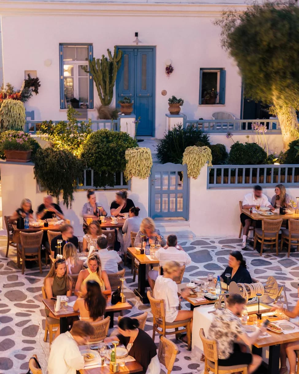 Guests enjoying dinner on d'angelo's terrace at dusk beside a whitewashed Cycladic courtyard